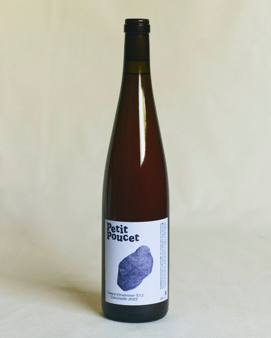 A slender brown Alsace wine bottle with a minimalist white label bearing the words “Petit Poucet” alongside a delicate white illustration featuring a nice stone and the text “Gewurtztraminer STZ 
Macération 2022”