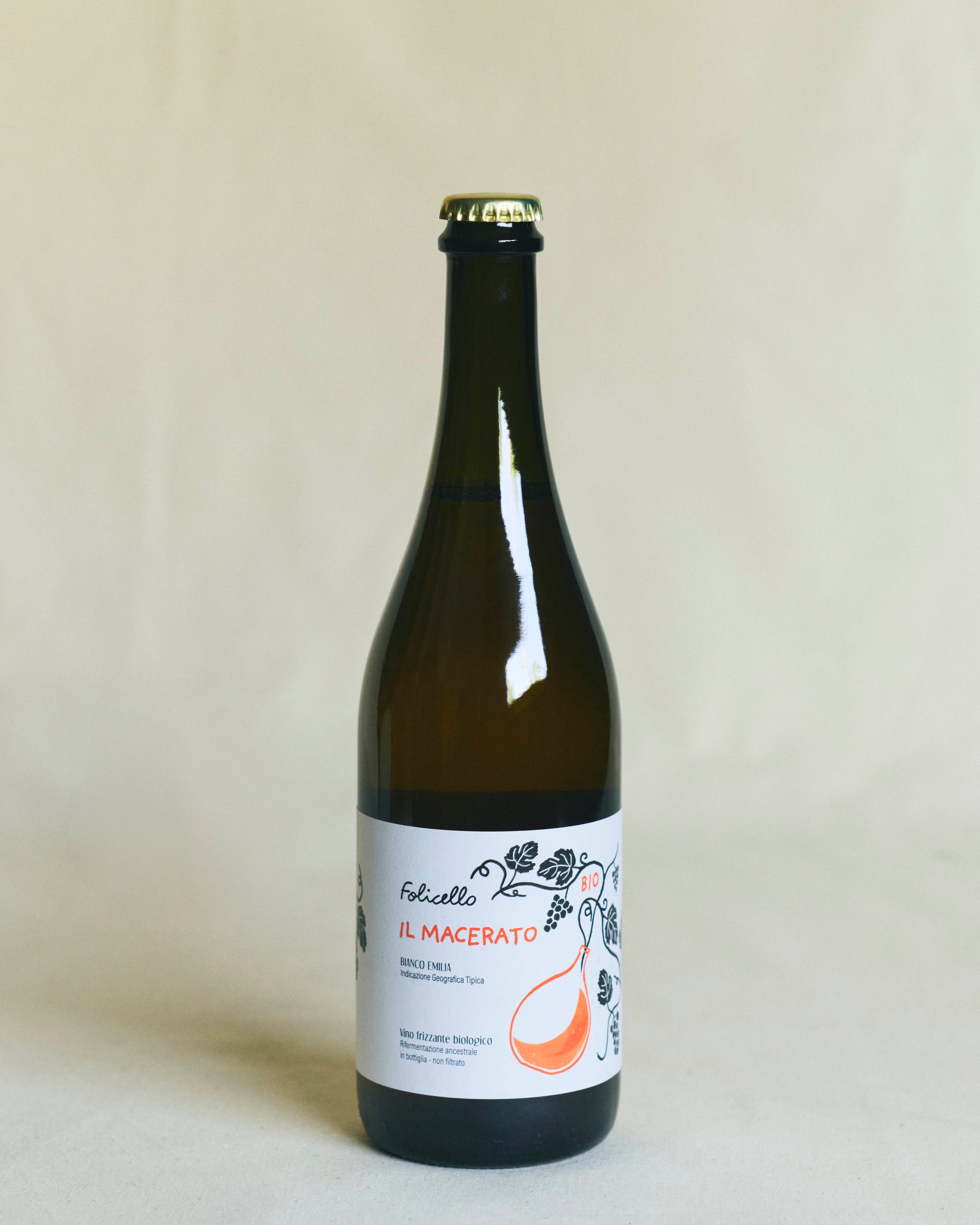 A brown bottle of wine, sealed with a metal crown cap. The white label reads “Folicello Il Macerato” and features illustrations of grapes and flowers in orange lettering.